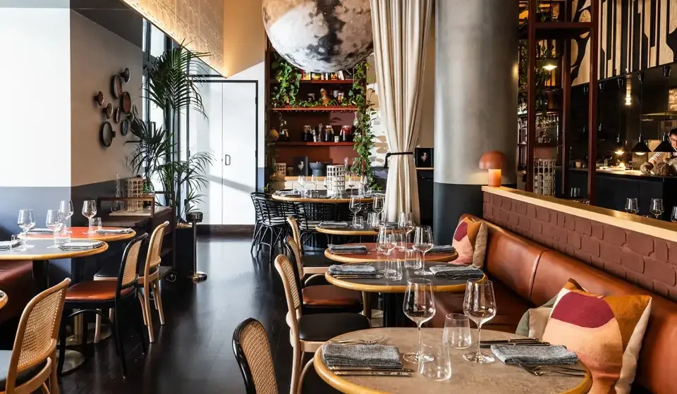 Jana Restaurant at QT Newcastle: dining room with round timber tables, leather banquettes and a large moon sculpture overhead