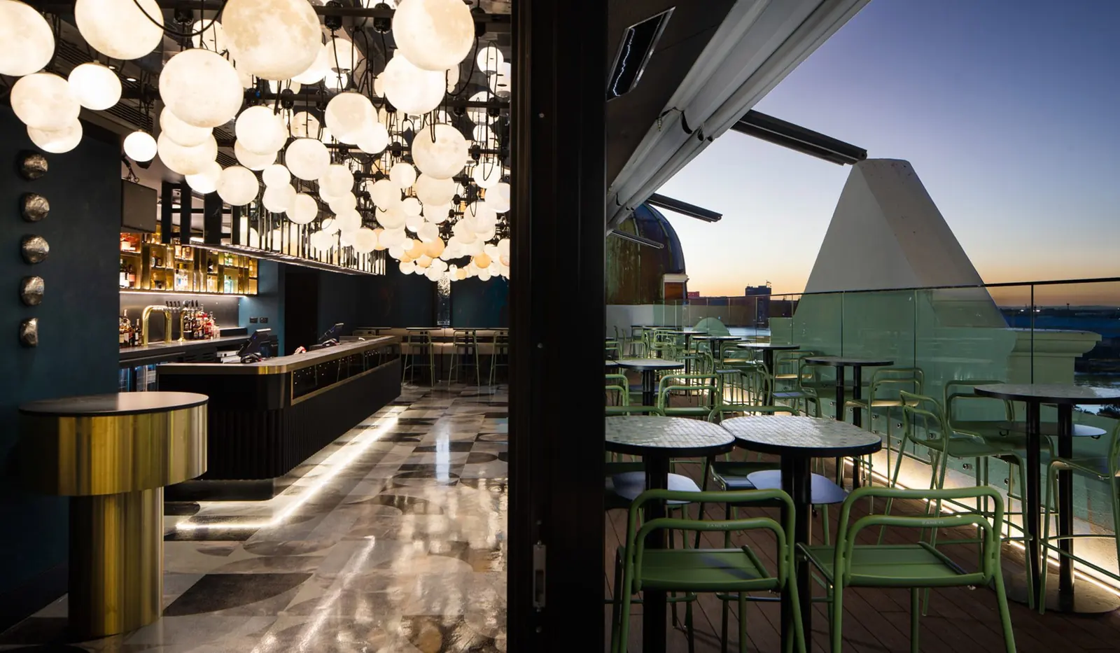 QT Newcastle rooftop bar at night: a canopy of globe pendant lights over the bar, with the terrace beyond